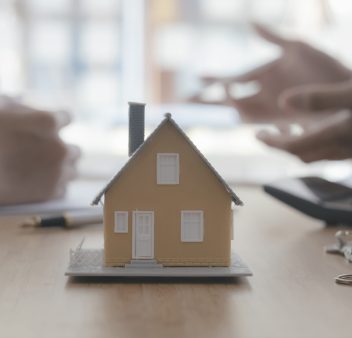 Close up house model on blur background of real estate agent and customer. Business and finance of buy sell and rent real estate concept.